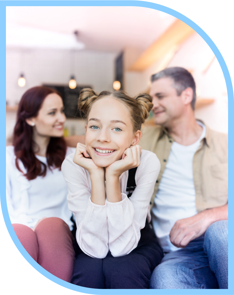 Foto auf dem ein junges Mädchen um die 13 Jahre abgebildet ist und in die Kamera lächelt, dahinter unscharf die Eltern im Hintergrund